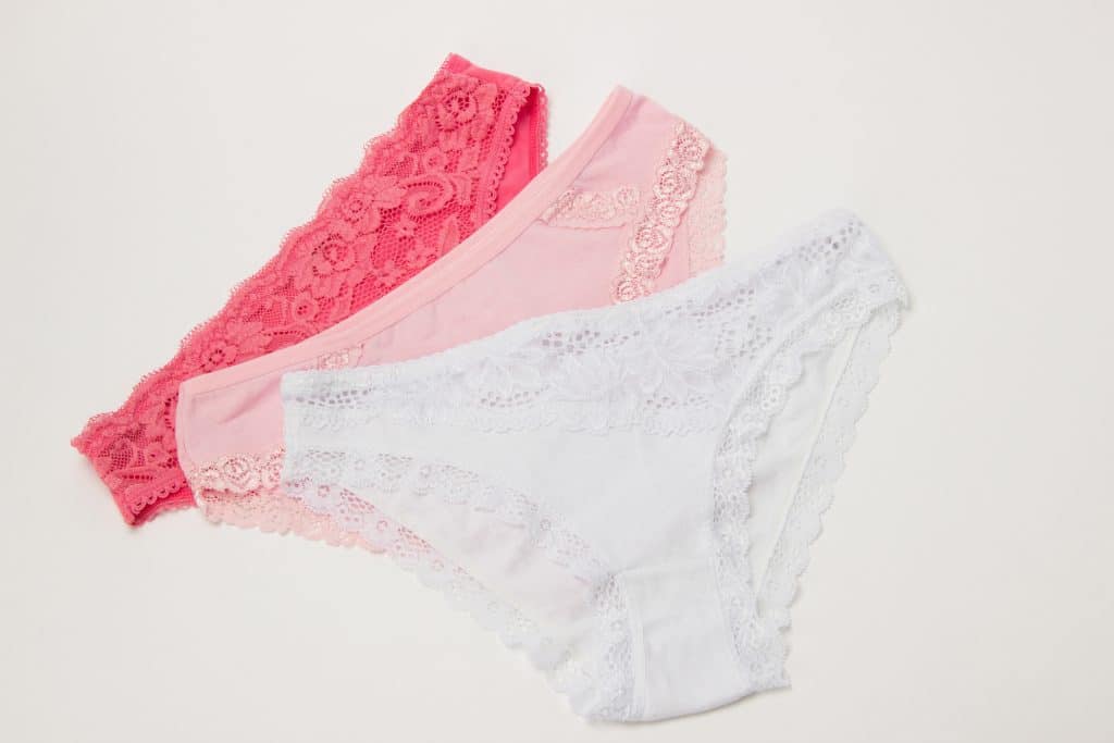 Trois paires de sous-vêtements en dentelle pour femmes aux couleurs rose et blanc disposées sur un fond clair.