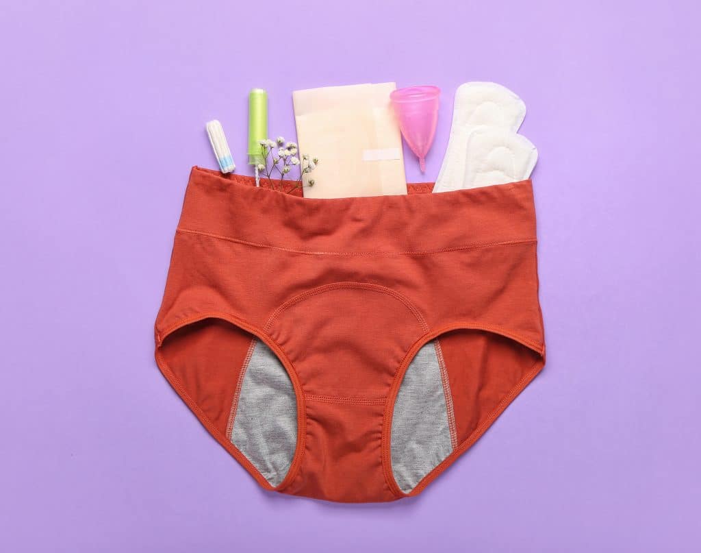 Produits d'hygiène menstruelle disposés à l'intérieur d'une paire de sous-vêtements sur fond violet.