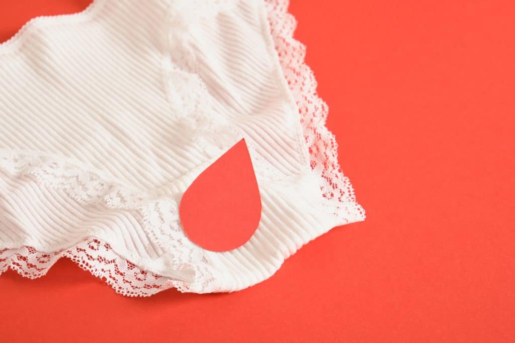 Une serviette menstruelle blanche avec un symbole de goutte rouge sur fond rouge vif.